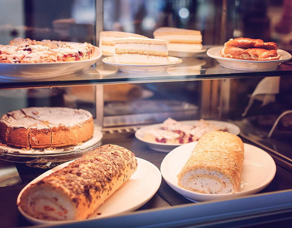 Vitrine mit verschiedenen Kuchen und Gebäckstücken wie Blechkuchen, Sahneschnitten und Rouladen auf Tellern.