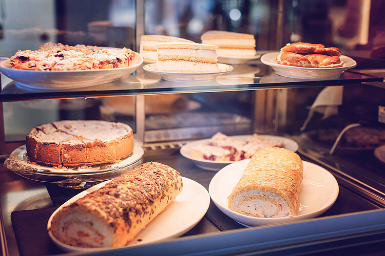 Lemp’s Genussgarten Kuchen Vitrine mit verschiedenen Kuchen und Gebäckstücken wie Blechkuchen, Sahneschnitten und Rouladen auf Tellern.
