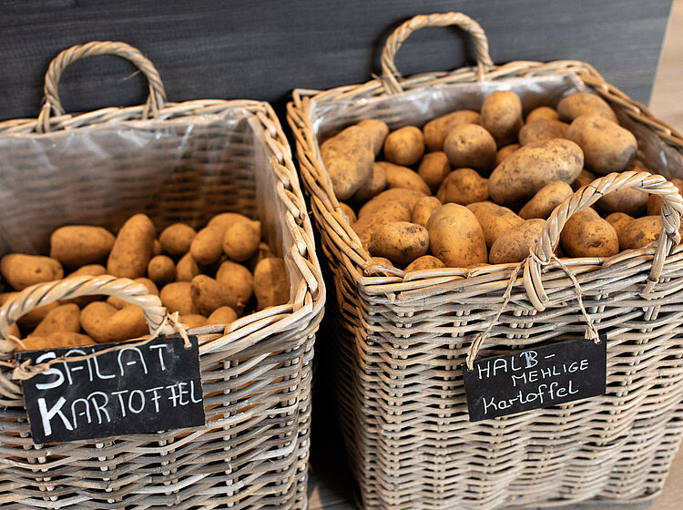 Zwei geflochtene Körbe mit Kartoffeln, beschildert als Salatkartoffeln und halb-mehlige Kartoffeln.