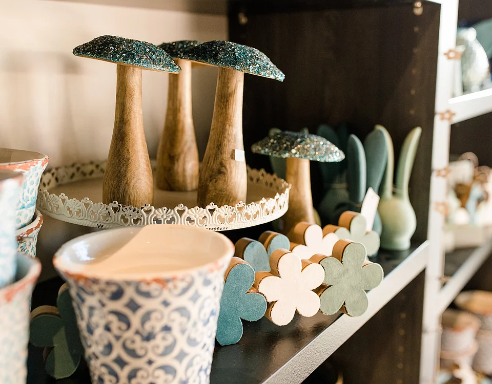 Regal mit dekorativen Holzpilzen, bemalten Blüten aus Holz und verzierten Keramikschalen.