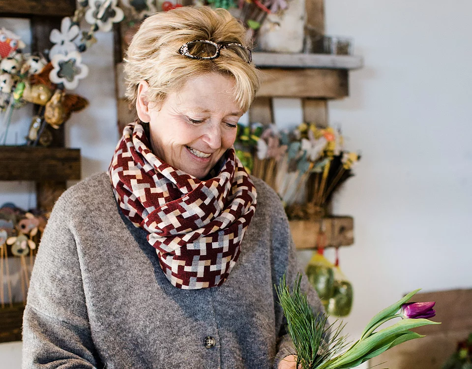 Ältere Frau schneidet Blumen und grüne Zweige in einem Blumenladen, um einen Strauß zu binden.