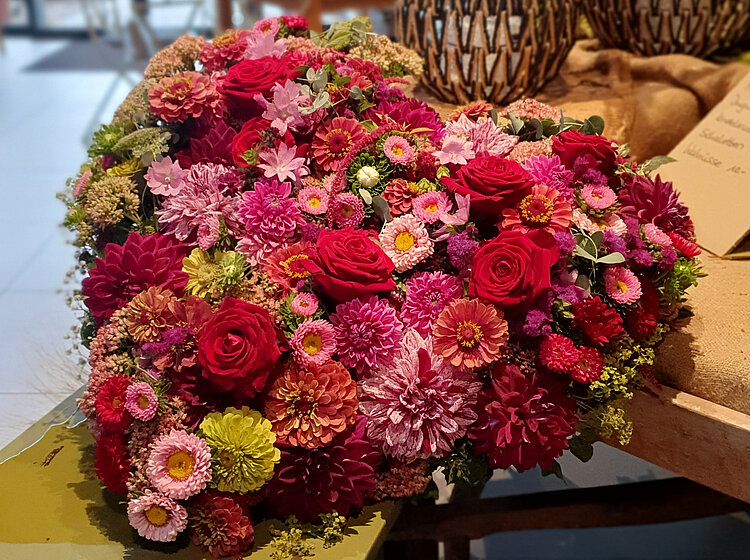 Buntes Herz aus verschiedenen Blumen in einem Laden, im Hintergrund Dekorationsgegenstände und Pflanzen.